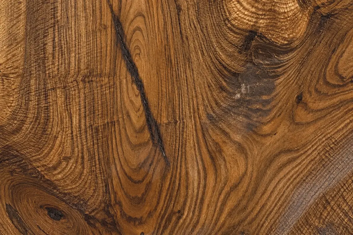 Close-up of figured Bastogne walnut — swirling honey and chocolate grain around a knot, with a long dark check running through it