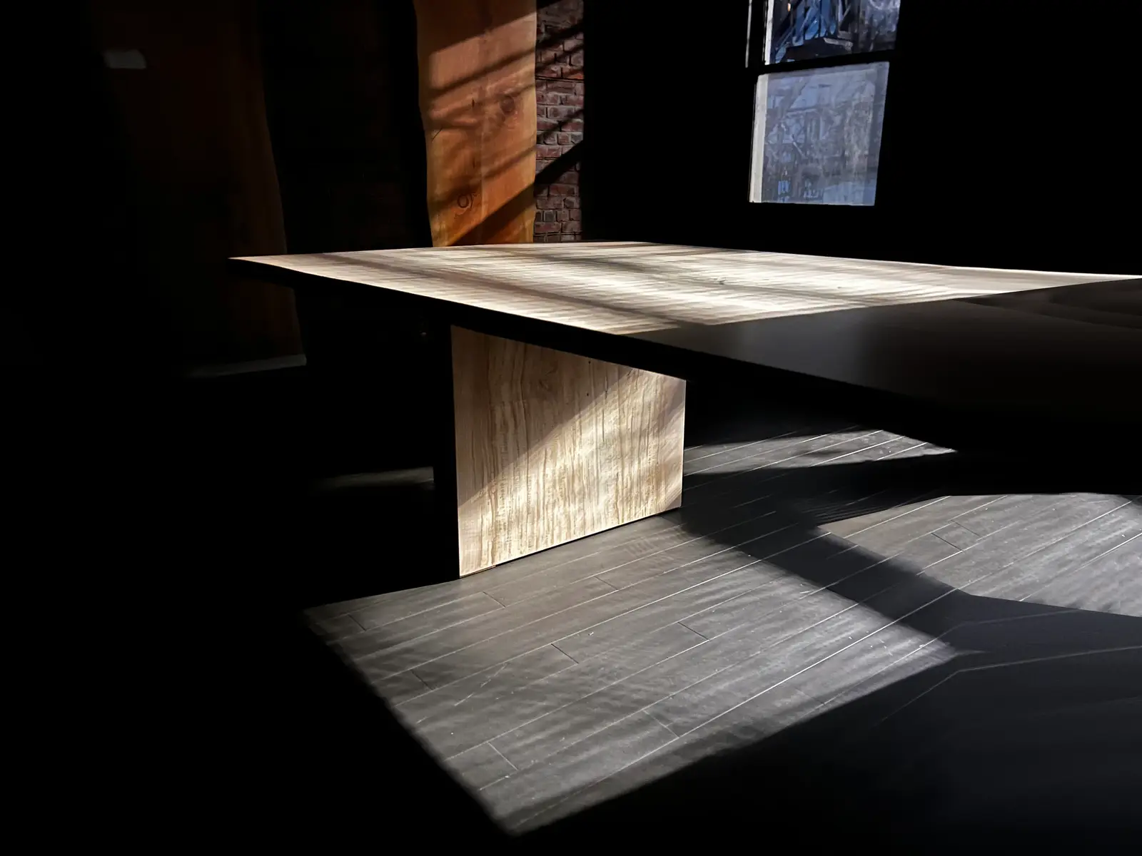 Curly maple table catching a beam of window light in the dark studio