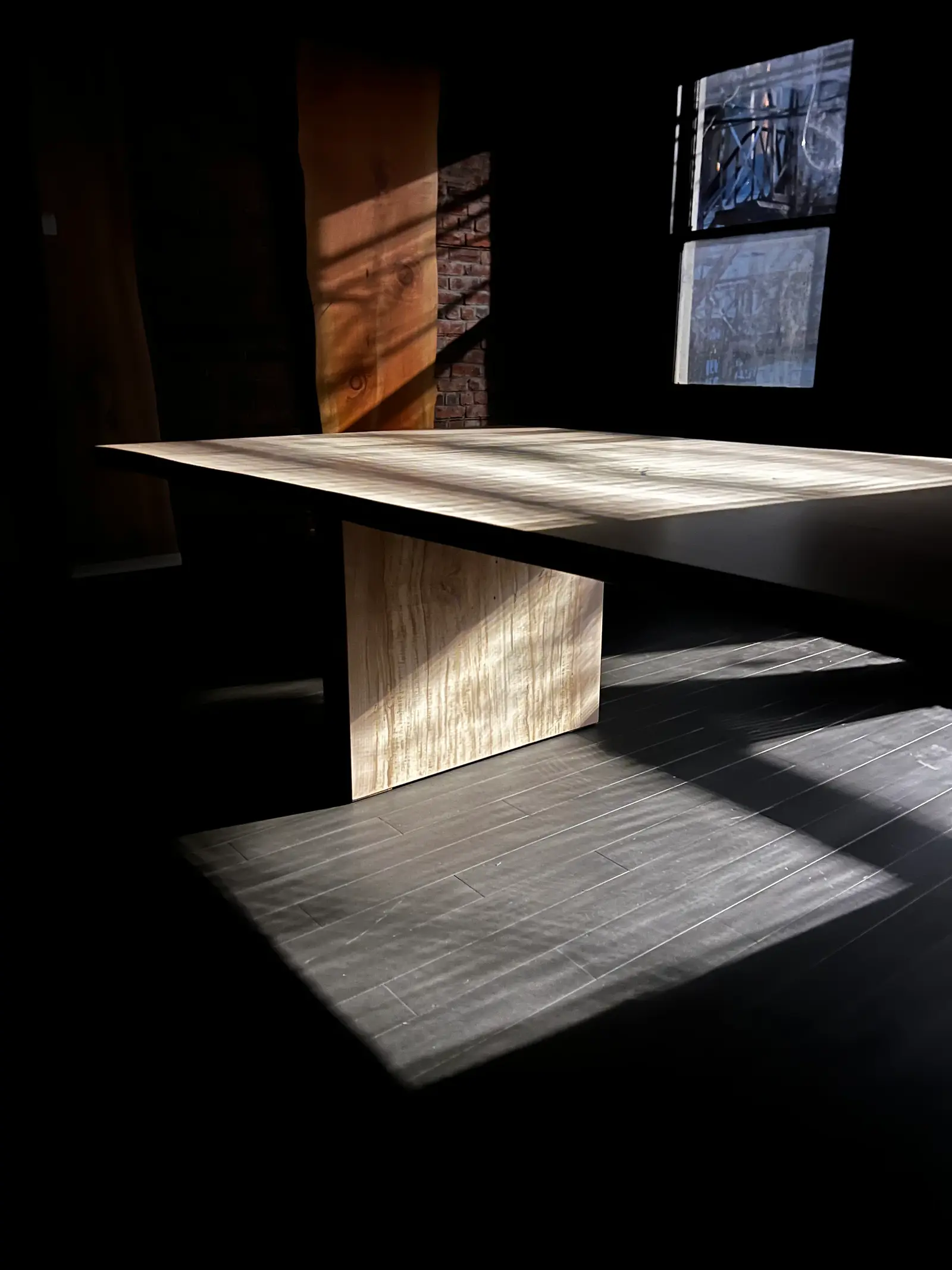 Spalted maple table in raking window light against a brick wall