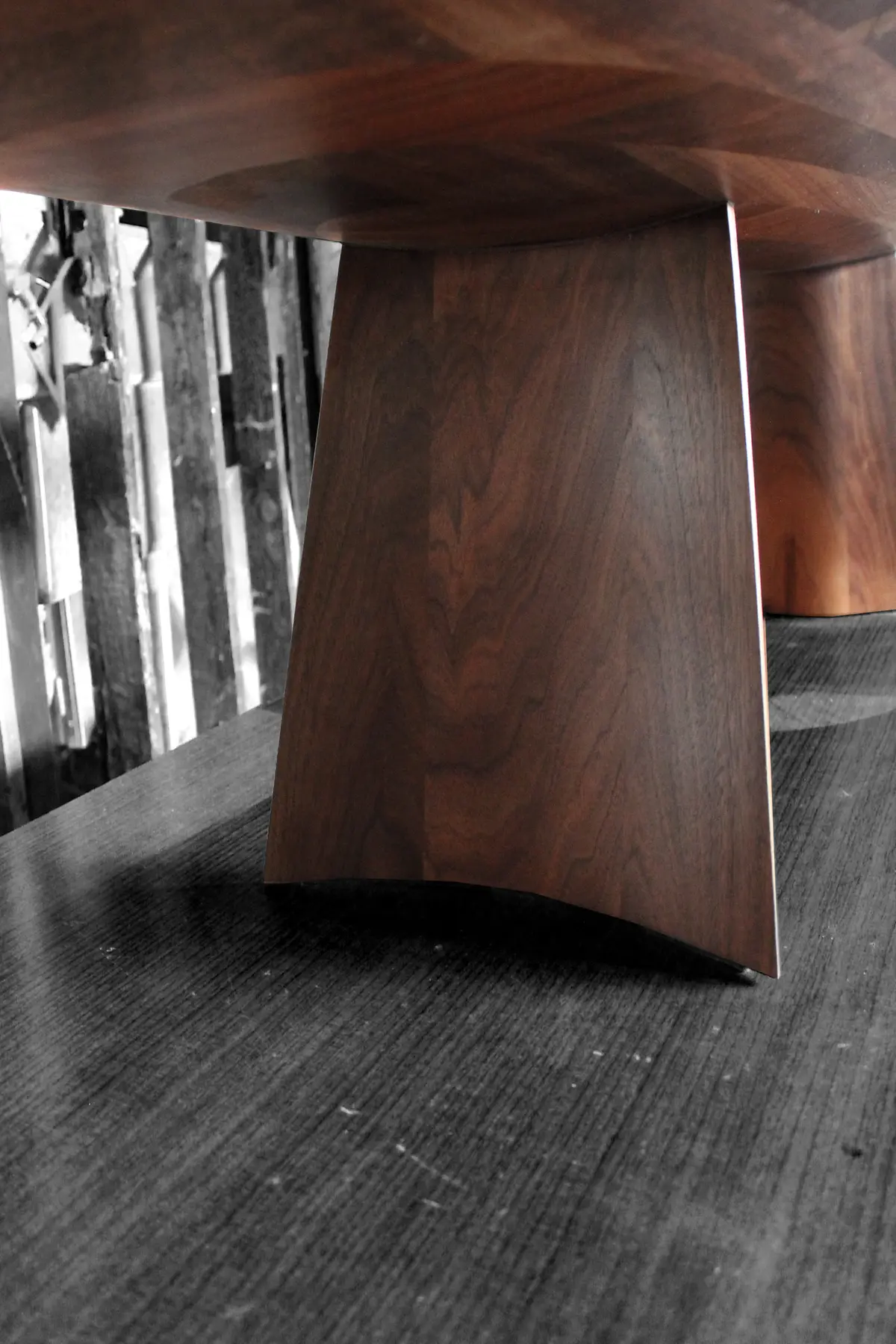 The sculpted base of a walnut Swell table, its curved blade rising to meet the underside of the top