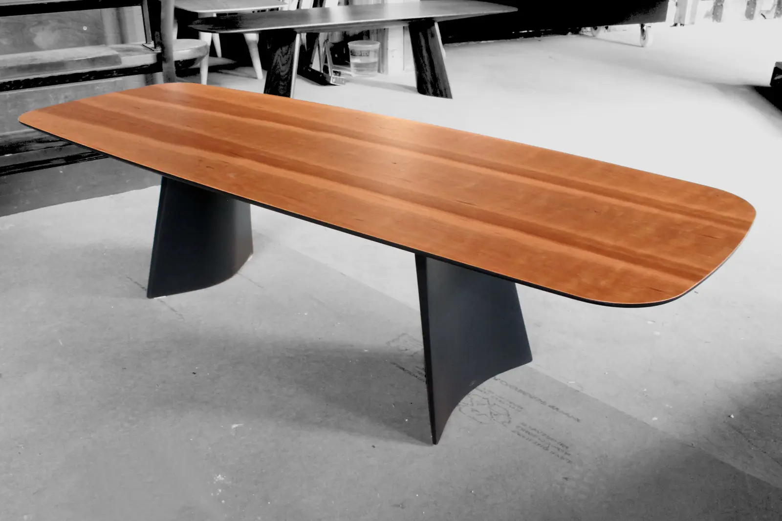 A Swell dining table with a warm reddish top on two black flared bases, photographed on the shop floor