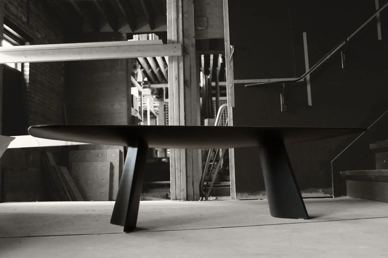 A blackened Swell table in profile, its thin top and flared legs silhouetted against the timber framing of the studio