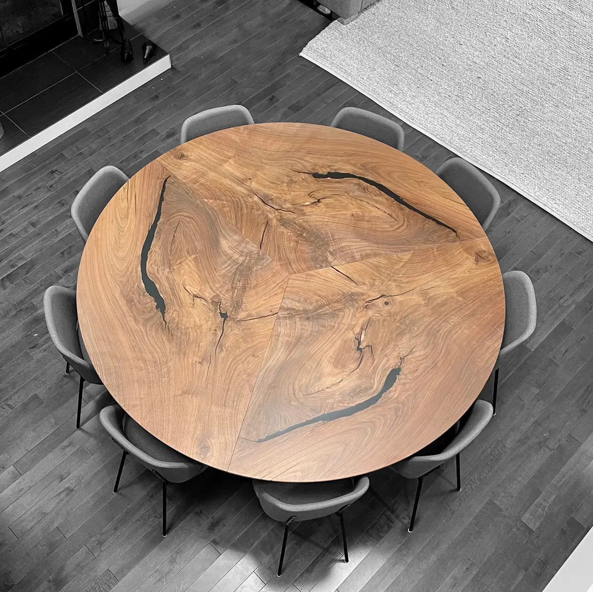A round Swell table in figured walnut seen from above, its book-matched segments and dark resin-filled fissures ringed by upholstered chairs