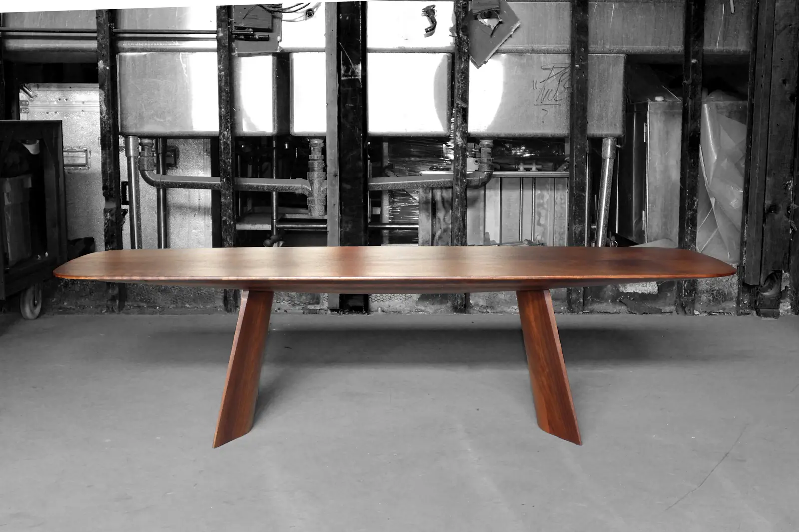 A walnut Swell dining table seen end-on in the shop, its blade-thin top edge running the full length above two angled legs